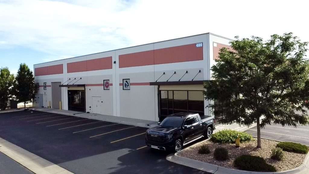 View of property for lease at 4880 Van Gordon Street in Wheat Ridge, Colorado. There are trees and a parking lot in the foreground with the building in the background.